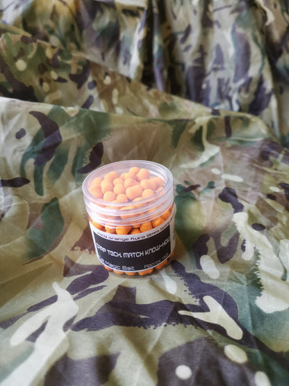 A clear plastic jar containing orange dumbbell shaped baits. label around the side reads 'AX89 orange fluro 8mm, carp tech, match know-how